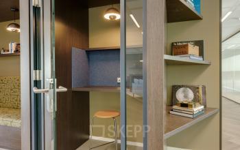 Furnished office to rent in Amsterdam South East, Herikerbergweg 288, featuring a cozy work nook with a stool and shelves integrated into the modern design.