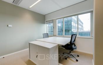 Furnished office space rental at Herikerbergweg 288, Amsterdam South East, featuring two modern desks with chairs and large windows overlooking the city.