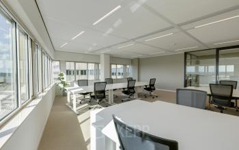 Bright office space rental in Amsterdam South East, featuring multiple desks and chairs with large windows allowing natural light.