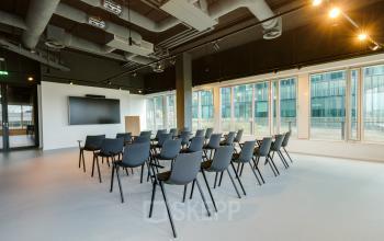 Spacious office to rent at Herikerbergweg 288, Amsterdam South East, featuring a furnished conference room with chairs arranged for presentations and large windows providing natural light.