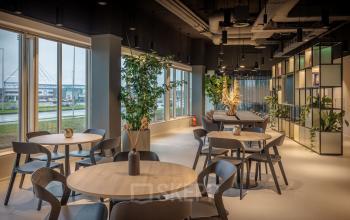 Spacious and modern workspace at Herikerbergweg 288 in Amsterdam South East featuring multiple wooden tables, large windows with a view, and lush greenery, perfect for office space rental.