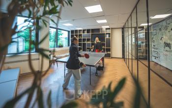 Two people playing table tennis in a well-lit office with wooden floors and large windows at Luttenbergweg 8, Amsterdam South East. Ideal for office space rental.