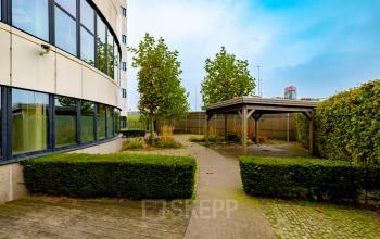 Exterior view of office building at Luttenbergweg 8, Amsterdam South East, featuring lush greenery and a sheltered outdoor seating area for employees. Ideal location for office space rental with natural surroundings.