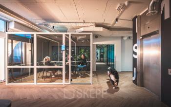 Modern office interior at Luttenbergweg 8, Amsterdam South East, featuring a meeting room with people engaged in discussion, highlighting a vibrant option for office space rental.