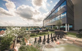 Modern office to rent at Luttenbergweg 8, Amsterdam South East, featuring an outdoor area with picnic tables and a large chessboard set against a reflective building facade.