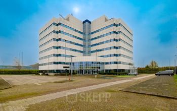 Exterior view of a modern office building located at Luttenbergweg 8, Amsterdam South East, featuring a spacious parking area, perfect for businesses seeking office space rental.