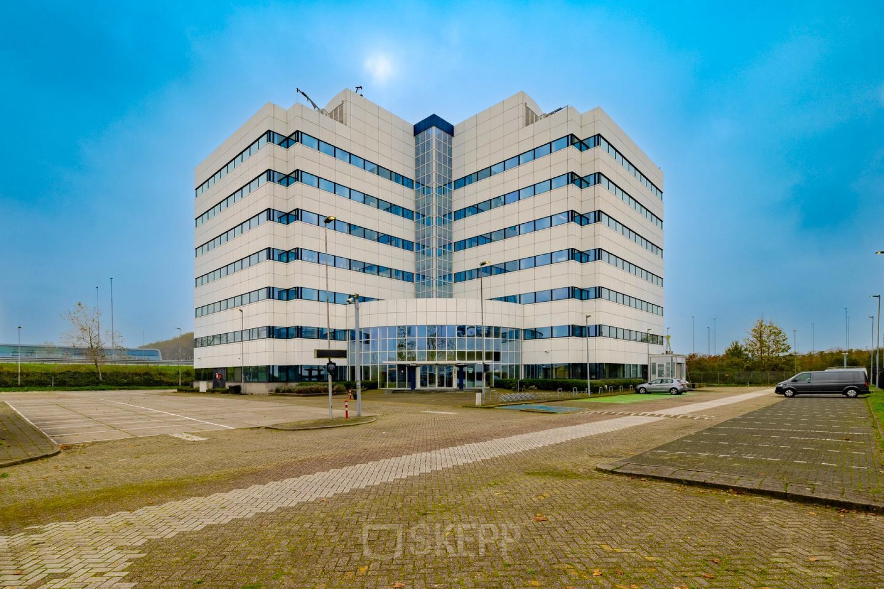 Exterior view of a modern office building located at Luttenbergweg 8, Amsterdam South East, featuring a spacious parking area, perfect for businesses seeking office space rental.