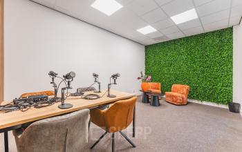 Furnished office space at Paasheuvelweg 20, Amsterdam South East, featuring a modern meeting table with microphones and vibrant chairs against a backdrop of a green wall.