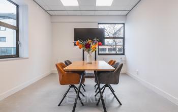 Bright office space featuring a wooden table with chairs, located at Paasheuvelweg 20. Ideal office space rental in Amsterdam South East. Large windows offer natural light.