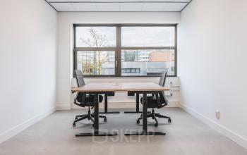 Bright office space at Paasheuvelweg 20, Amsterdam South East, featuring two desks and chairs near a large window. Ideal for office space rental.
