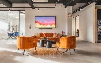 Modern office lounge area at Paasheuvelweg 20, Amsterdam South East with stylish seating, a central coffee table, and a mounted TV. Ideal space for office space rental.