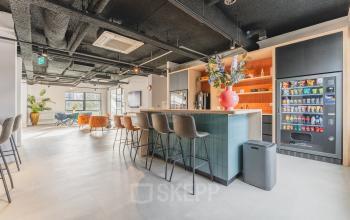 Modern office space to rent at Paasheuvelweg 20, Amsterdam South East, featuring a furnished interior with a stylish open floor plan, a large central island, vending machine, and seating area for relaxation.