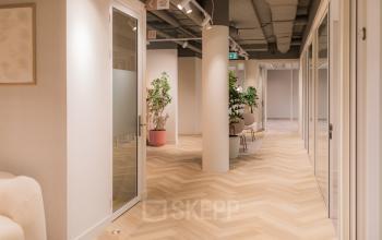 Interior view of a modern office space at Hullenbergweg 109-135, Amsterdam South East, showcasing a clean corridor with glass doors and potted plants, available for office space rental.