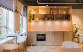 Modern furnished pantry with light wood cabinets, open shelves, and a small round table. Ideal for office space rental in Amsterdam South East.