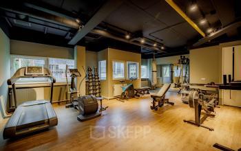 Modern gym area in an office space rental at Hogehilweg 8, Amsterdam South East, with various fitness equipment and wooden flooring.