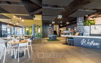 Modern office lounge at Hogehilweg 8, Amsterdam South East, with seating areas, a coffee bar, and vibrant decor.