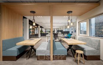 Modern office interior at Hogehilweg 8 in Amsterdam Zuid-Oost featuring two booth seating areas, open workspaces in the background, and large windows providing natural light.