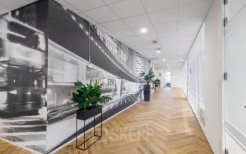 Modern office corridor at Karspeldreef 8, Amsterdam South East with stylish black and white wall art, herringbone flooring, and potted plants.