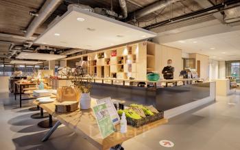 Interior of an office to rent at Karspeldreef 8, Amsterdam South East, featuring a modern pantry and open workspaces with individuals engaging in work-related activities.