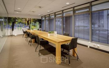 Modern conference room in Karspeldreef 8, Amsterdam South East, with a long wooden table, chairs, and large windows providing natural light.