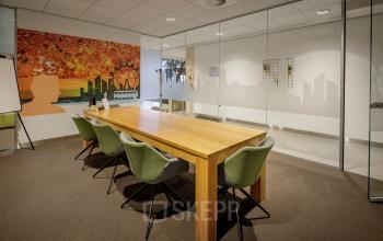 Modern office space rental at Karspeldreef 8, Amsterdam South East, featuring a spacious meeting room with a large wooden table, green chairs, and a vibrant wall mural.