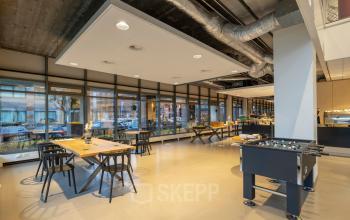 Modern office space with large windows, wooden tables, and a foosball table at Karspeldreef 8, Amsterdam South East.