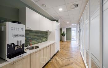 Modern pantry area in an office space rental at Karspeldreef 8, Amsterdam South East, featuring sleek cabinetry, a coffee machine, and bright lighting.