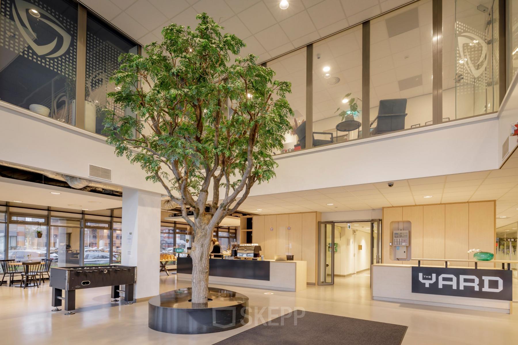 Open and inviting office reception area at Karspeldreef 8, Amsterdam South East, featuring a central indoor tree, modern seating, and a welcoming front desk, ideal for office space rental.