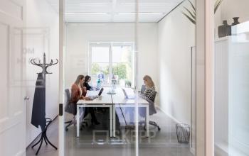 Modern office space rental in Amsterdam South East at Burgemeester Stramanweg 102, featuring a bright, glass-enclosed workspace with three professionals working at laptops around a table.