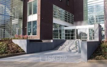 Exterior view of office building at Burgemeester Stramanweg 102, Amsterdam South East, featuring a modern facade with large glass windows and a path leading to the entrance.