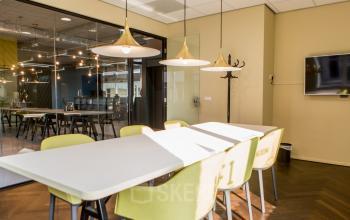 Modern conference room with large table, yellow chairs, and stylish lighting at Burgemeester Stramanweg 102, Amsterdam South East, available for office space rental. The space features glass walls and a mounted TV screen.