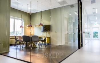Modern conference room at Burgemeester Stramanweg 102, Amsterdam South East, featuring sleek glass walls, stylish lighting, and a large meeting table with chairs, ideal for office space rental.
