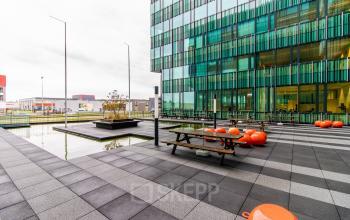 Outdoor area at Herikerbergweg 292, Amsterdam South East, ideal for taking breaks during an office space rental. Features seating and a modern façade.