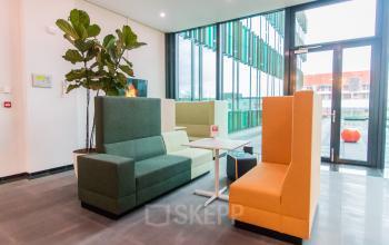 Modern office space rental in Amsterdam South East with vibrant seating area, large windows, and natural light.