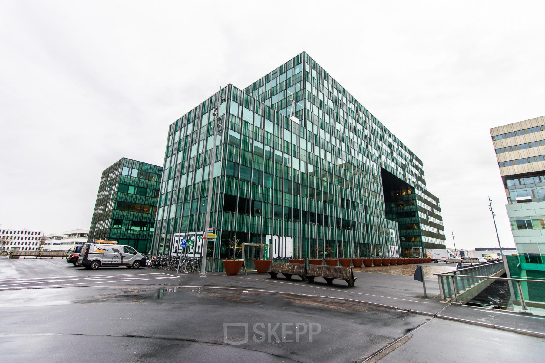 Exterior view of a modern glass building at Herikerbergweg 292, offering office space rental in Amsterdam South East.