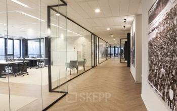 Modern office space with glass-walled meeting rooms, wooden floors, and natural lighting located at De Entree 99-197, Amsterdam South East.