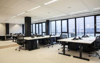 Spacious office area at De Entree 99-197 in Amsterdam South East, featuring multiple workstations with ergonomic chairs, large windows, and ample natural light.