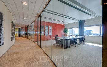 Modern office space at De Entree 99-197, Amsterdam South East, featuring a glass-walled conference room with a large table and chairs, ideal for office space rental.