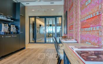 Interior view of an office space at De Entree 99-197, Amsterdam South East with a stylish lounge area featuring vibrant decor and a coffee station, ideal for office space rental.