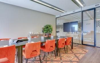 Bright conference room with red chairs, large table, and a TV for presentations, ideal for office space rental in Amsterdam South East.