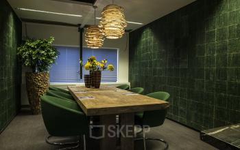 Conference room with a wooden table, green chairs, pendant lights, and a large window at De Entree 99-197, Amsterdam South East. Office space rental available.
