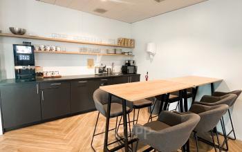 Modern pantry with wooden flooring, tall counter and chairs, kitchen equipment, and shelves at De Entree 230, Amsterdam South-East; ideal for short breaks during office space rental.