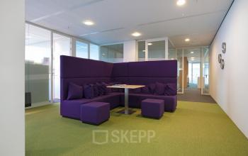 Chic office space rental at Parnassusweg 819, Amsterdam Zuidas, featuring a modern lounge area with plush purple sofas and a vibrant green carpet.