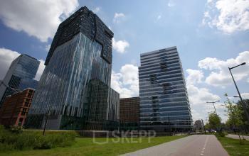 Modern office space rental at Parnassusweg 819, Amsterdam Zuidas, with a striking glass facade under a clear blue sky.