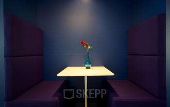 Elegant office space rental at Parnassusweg 819, Amsterdam Zuidas, featuring a private booth with purple seats and a single table highlighted by a vase of flowers.