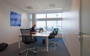 Modern office space rental at Parnassusweg 819, Amsterdam Zuidas, with a focused individual working at a desk with dual monitors and city views.
