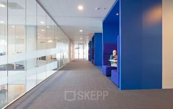 Modern office space rental at Parnassusweg 819, Amsterdam Zuidas with person in a private nook and glass-walled meeting rooms.