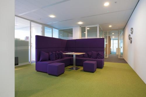 Chic office space rental at Parnassusweg 819, Amsterdam Zuidas, featuring a modern lounge area with plush purple sofas and a vibrant green carpet.