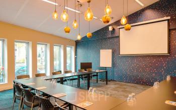 Modern conference room at Jachthavenweg 109-A, Amsterdam Zuidas, featuring a large table, chairs, projector, and decorative lighting.