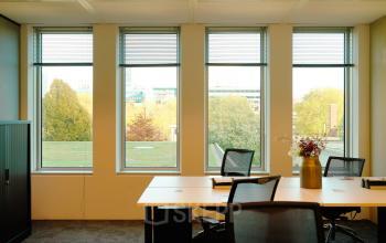 Bright office space with large windows and a view of Amsterdam Zuidas at Jachthavenweg 109-A, featuring modern furniture and a floral centerpiece.
